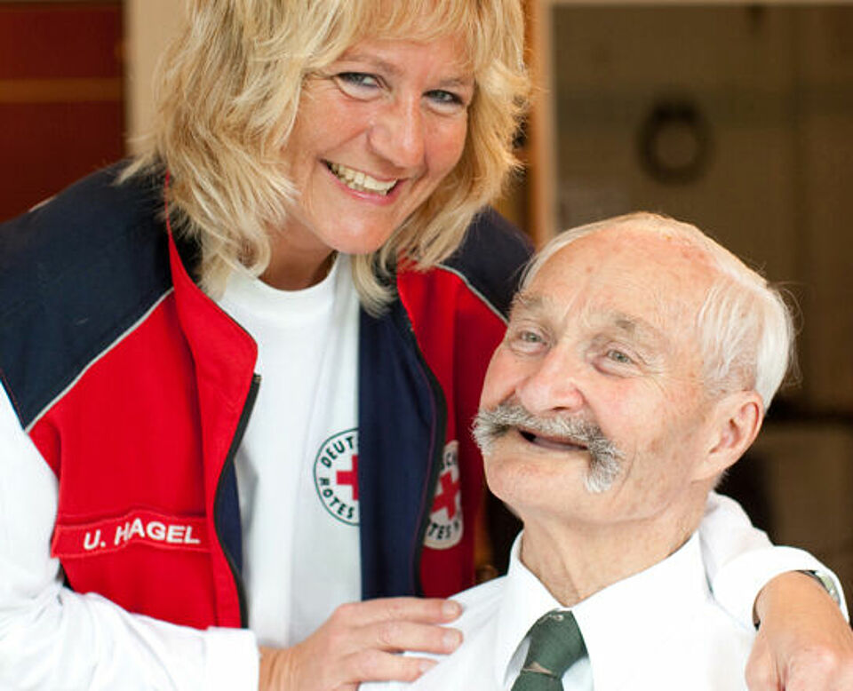 Ein lachender Senior mit einer DRK Mitarbeiterin. 